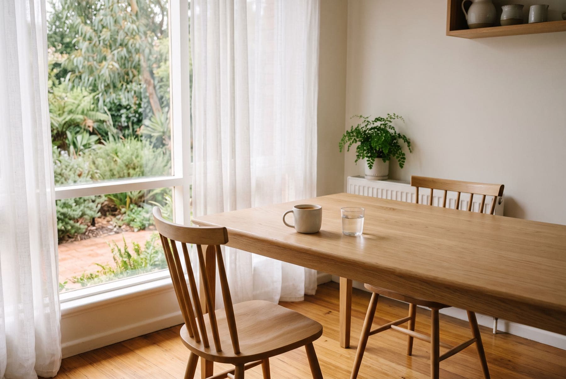 A kitchen table with two chairs pulled out, morning light across the timber
